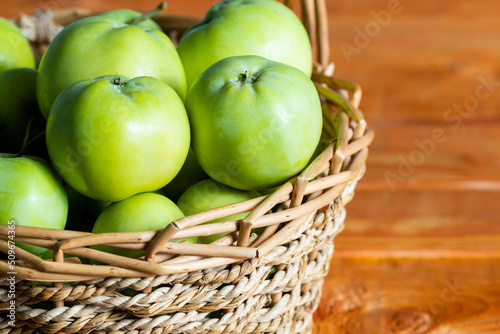 Composition with juicy green apples in wicker basket on table. Copy space