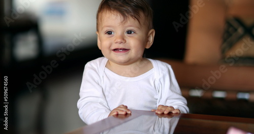 Adorable baby hiding under table. Infant boy smiling to camera portrait playing peekaboo