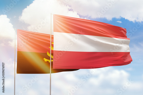 Sunny blue sky and flags of austria and angola
