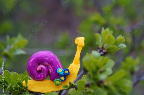 Snail figurine decorated with a flower on a background of green grass. Springtime.