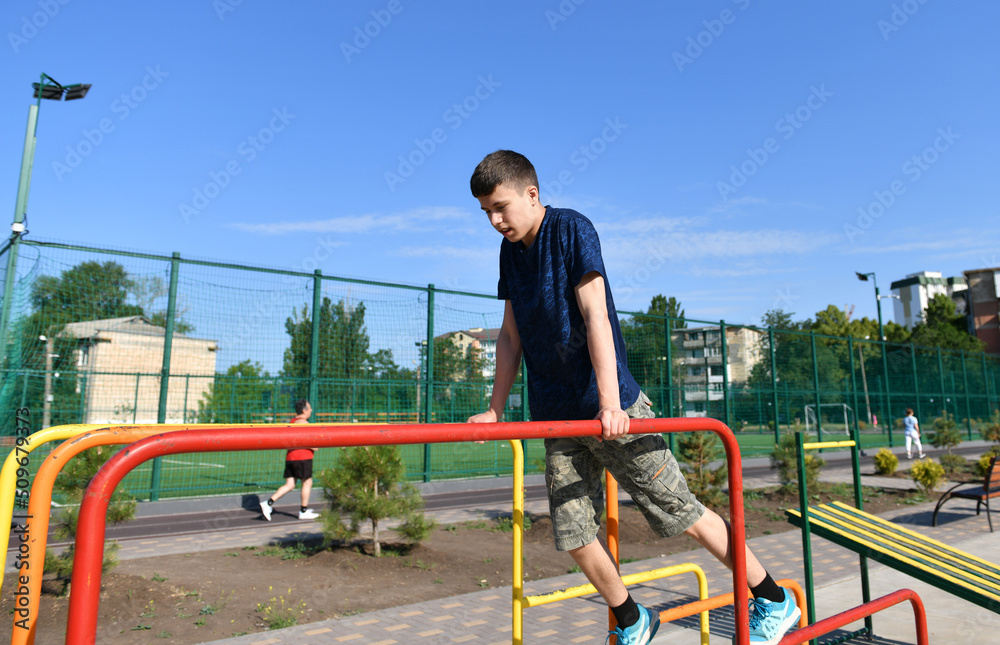 Fototapeta premium a teenage boy trains on a sports ground outdoors, he does physical exercises, a healthy lifestyle, a bright sunny day in summer