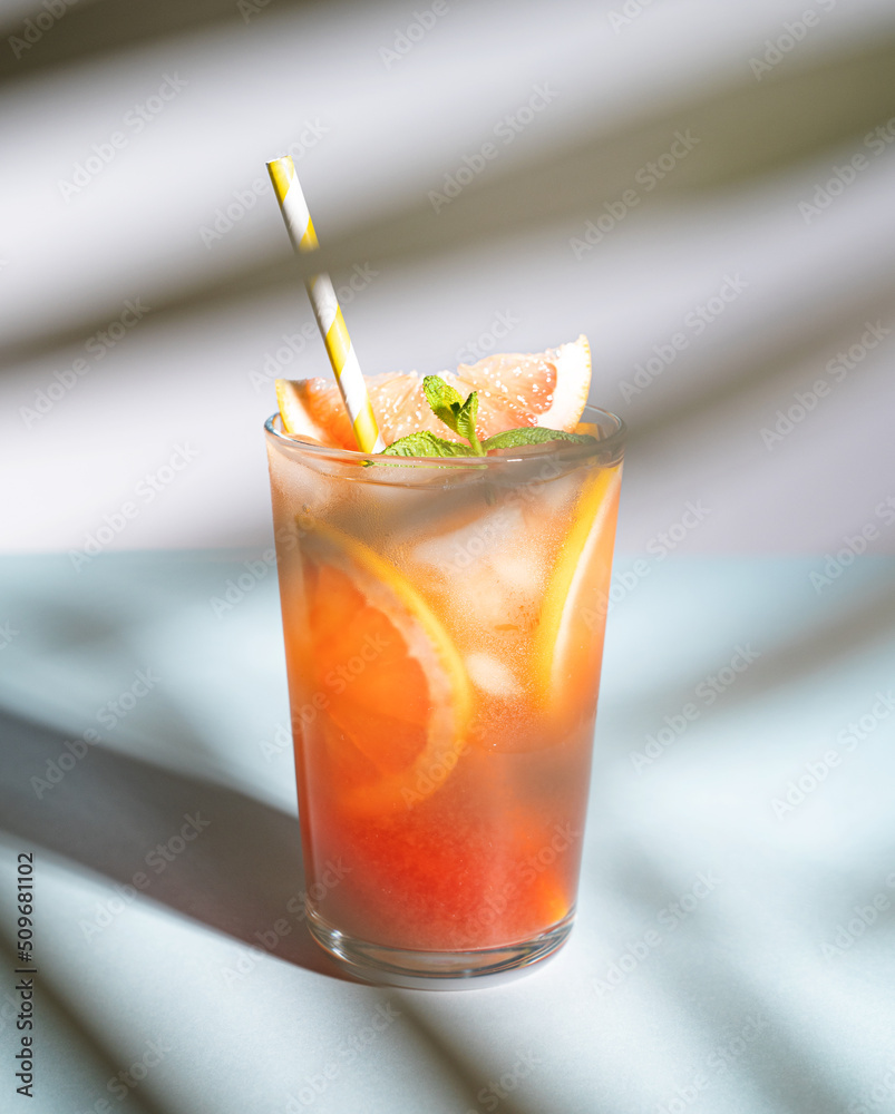 Fresh grapefruit juice with ice, mint and grapefruit slice in a glass on a blue background with shadows. Front view Fresh grapefruit juice with ice, mint and grapefruit slice in a glass on a blue background with shadows. Front view