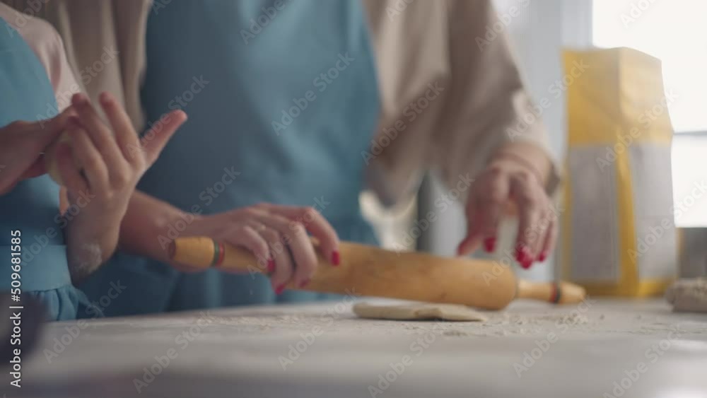 housewife is rolling out dough with rolling pin in kitchen, little daughter is helping to mother housewife is rolling out dough with rolling pin in kitchen, little daughter is helping to mother