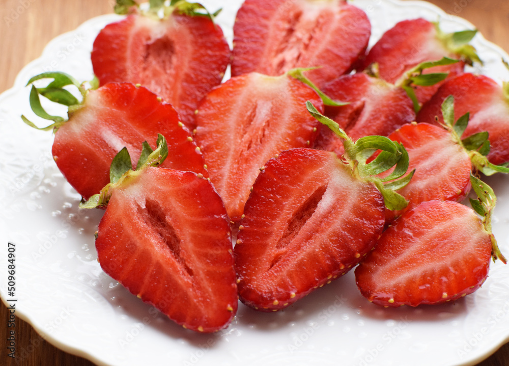 Ripe juicy strawberries cut in halves on a white plate.