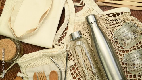 Zero waste eco friendly reusable objects such as reusable linen shopping bags, glass jars and wooden toothbrushes on wooden background, top view, rotating