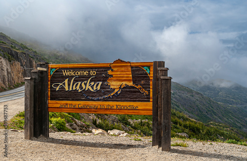 Skagway, Alaska, USA - July 20, 2011: Klondike highway to Canada. Colorful Welcome sign near the border. Cloudscape in back. photo