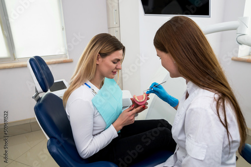 a woman dentist shows a young girl a model of an artificial jaw.