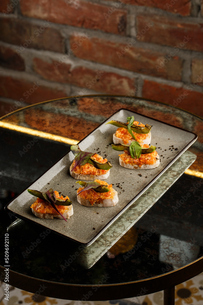baked bruschetta with salmon, cheese, sun-dried tomatoes and avocado in gray plate on bright background