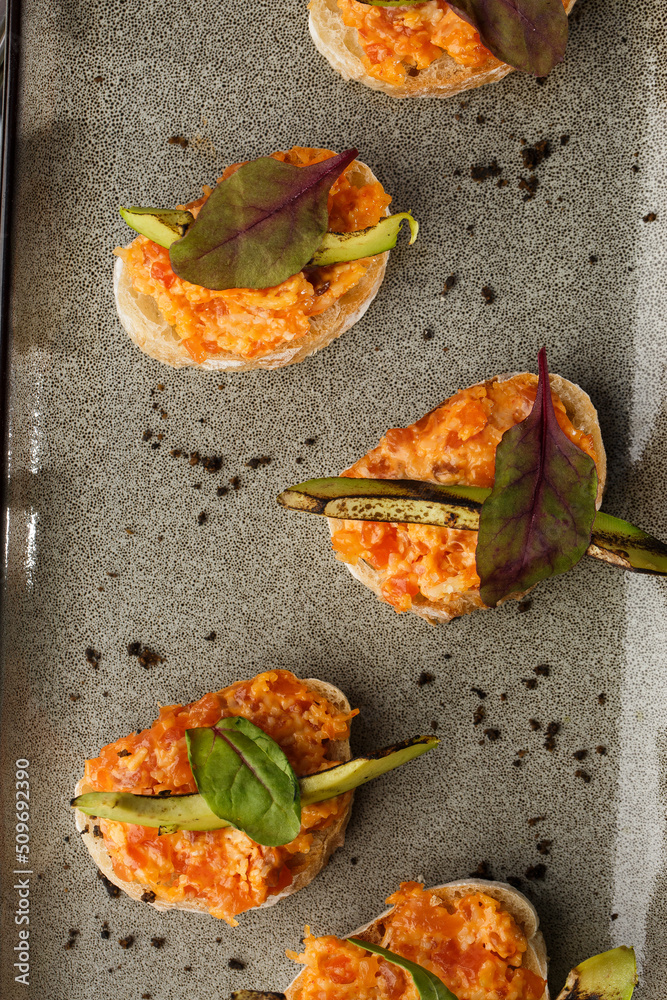 baked bruschetta with salmon, cheese, sun-dried tomatoes and avocado in gray plate on bright background
