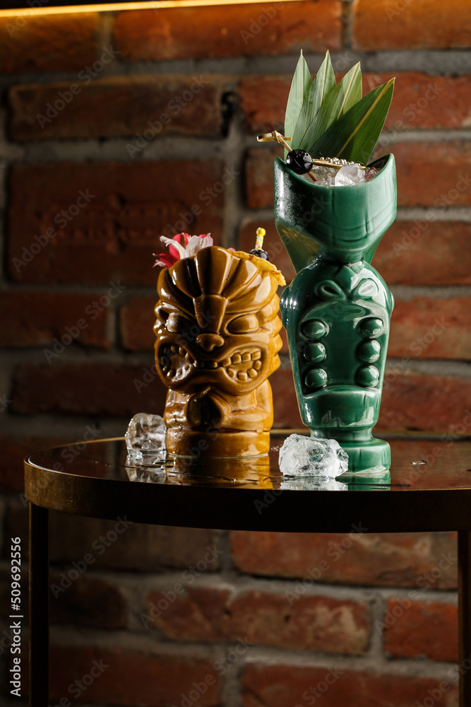 Tiki Drink Cocktails. Two cocktails in different glasses against the background of a bar decorated with dried fruits and tropical leaves.