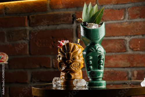 Obraz na płótnie Tiki Drink Cocktails. Two cocktails in different glasses against the background of a bar decorated with dried fruits and tropical leaves. w salonie