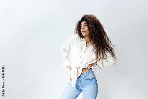 Sexy Curly Pretty Pensive Latin Female Lady in White Shirt Holding Hands On Waist copy space, free place Looking Aside Isolated At White Studio Wall Background. Good Offer, Banner, Mockup