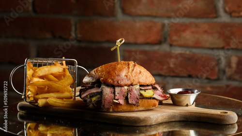Obraz na płótnie Pastrami sandwich on rye bread served with pickles and mustard sauce. Tasty sandwich with french fries potatoes on dark background. w salonie