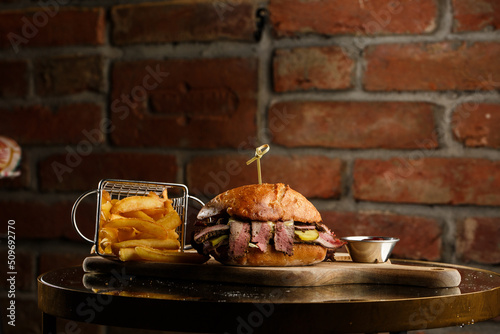 Obraz na płótnie Pastrami sandwich on rye bread served with pickles and mustard sauce. Tasty sandwich with french fries potatoes on dark background. w salonie