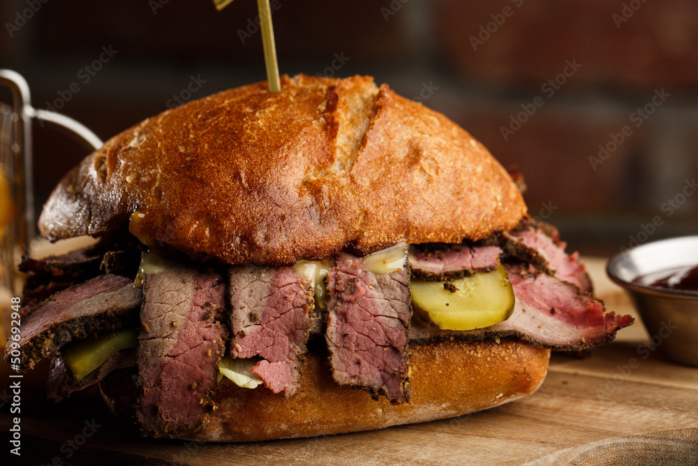 Pastrami sandwich on rye bread served with pickles and mustard sauce. Tasty sandwich with french fries potatoes on dark background.