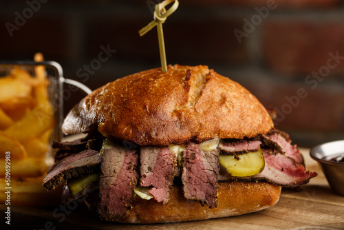 Obraz na płótnie Pastrami sandwich on rye bread served with pickles and mustard sauce. Tasty sandwich with french fries potatoes on dark background. w salonie