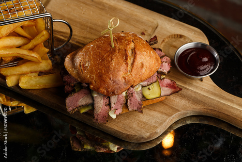 Obraz na płótnie Pastrami sandwich on rye bread served with pickles and mustard sauce. Tasty sandwich with french fries potatoes on dark background. w salonie