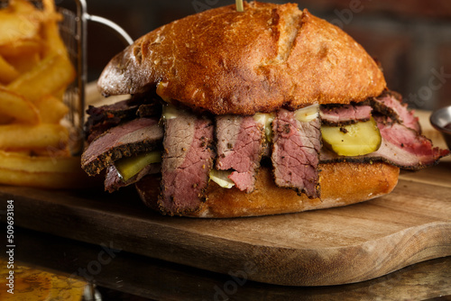 Obraz na płótnie Pastrami sandwich on rye bread served with pickles and mustard sauce. Tasty sandwich with french fries potatoes on dark background. w salonie