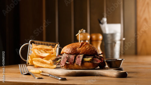 Obraz na płótnie Pastrami sandwich on rye bread served with pickles and mustard sauce. Tasty sandwich with french fries potatoes on dark background. w salonie