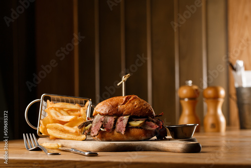 Obraz na płótnie Pastrami sandwich on rye bread served with pickles and mustard sauce. Tasty sandwich with french fries potatoes on dark background. w salonie