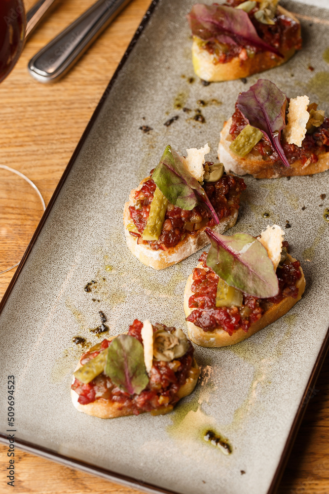 Four bruschettas with beef tartare on a plate, Crostini with Beef Tartare, beef Bruschetta, sandwich with raw gourmet beef.