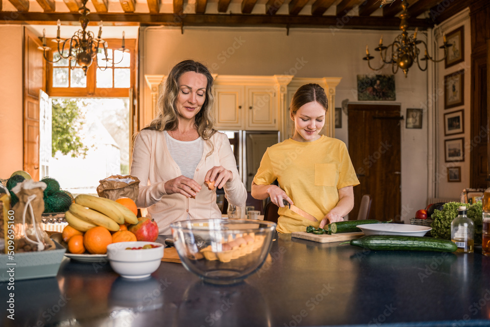 Calm adult woman smiling near her teenage daughter while cooking together