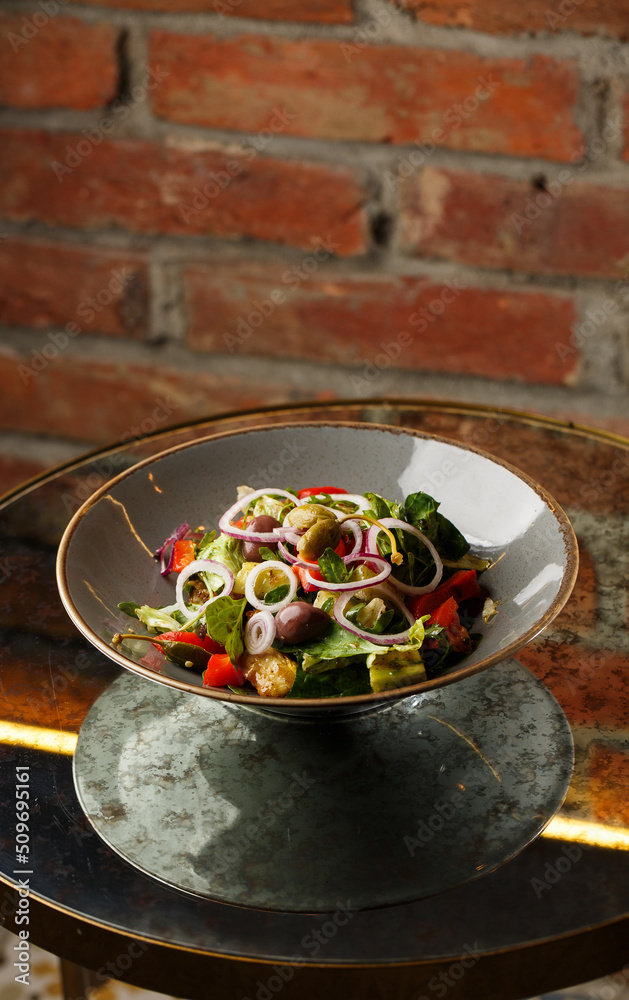 Greek salad with fresh vegetables: tomato, cucumber, red bel pepper, lettuce, onion, olives and cheese. Close-up on a white round plate on a wooden background. Salad menu with ingredients