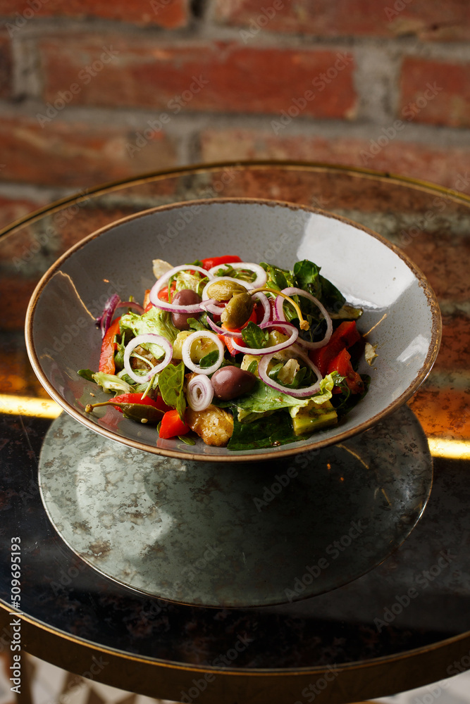 Greek salad with fresh vegetables: tomato, cucumber, red bel pepper, lettuce, onion, olives and cheese. Close-up on a white round plate on a wooden background. Salad menu with ingredients