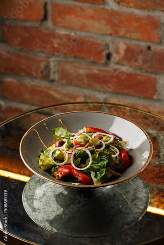 Obraz na płótnie Greek salad with fresh vegetables: tomato, cucumber, red bel pepper, lettuce, onion, olives and cheese. Close-up on a white round plate on a wooden background. Salad menu with ingredients w salonie