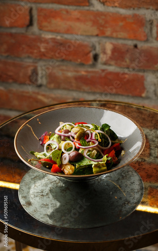 Greek salad with fresh vegetables: tomato, cucumber, red bel pepper, lettuce, onion, olives and cheese. Close-up on a white round plate on a wooden background. Salad menu with ingredients