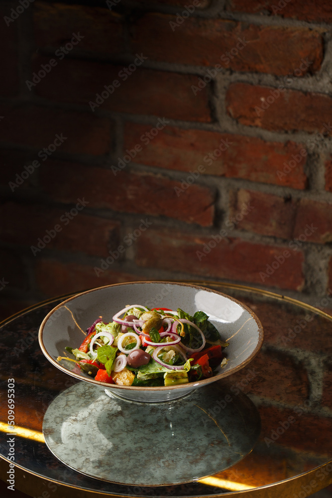 Greek salad with fresh vegetables: tomato, cucumber, red bel pepper, lettuce, onion, olives and cheese. Close-up on a white round plate on a wooden background. Salad menu with ingredients