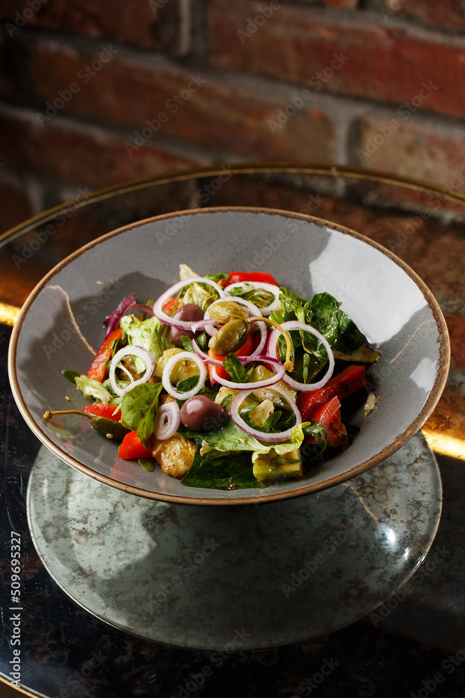 Greek salad with fresh vegetables: tomato, cucumber, red bel pepper, lettuce, onion, olives and cheese. Close-up on a white round plate on a wooden background. Salad menu with ingredients