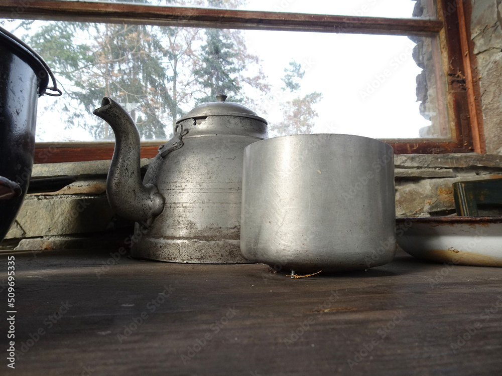 Old dilapidated aluminum teapot and pot standing on a dilapidated wooden table.