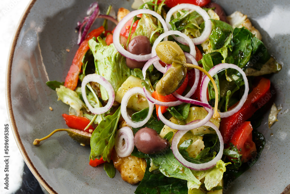 Greek salad with fresh vegetables: tomato, cucumber, red bel pepper, lettuce, onion, olives and cheese. Close-up on a white round plate on a wooden background. Salad menu with ingredients