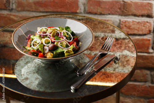 Obraz na płótnie Greek salad with fresh vegetables: tomato, cucumber, red bel pepper, lettuce, onion, olives and cheese. Close-up on a white round plate on a wooden background. Salad menu with ingredients w salonie