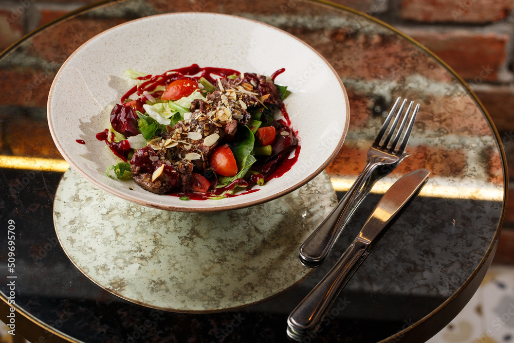 Salad with veal and tomatoes. Beef steak with raw vegetables mix side view. Grilled meat with garnish close-up. Delicious main course on table
