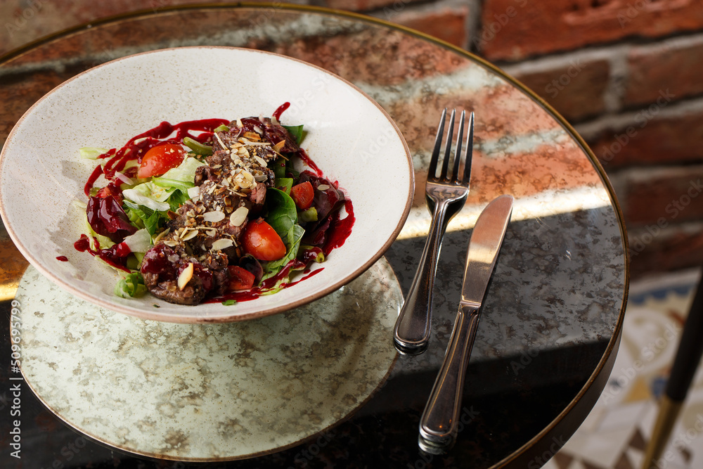 Salad with veal and tomatoes. Beef steak with raw vegetables mix side view. Grilled meat with garnish close-up. Delicious main course on table