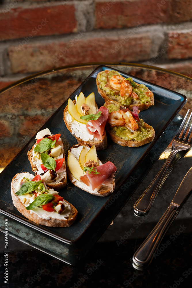 Bruschettas with vegetables. Start dishes with cherry tomatoes, avocado, cream cheese and shrimps. Food composition, tasty italian meal