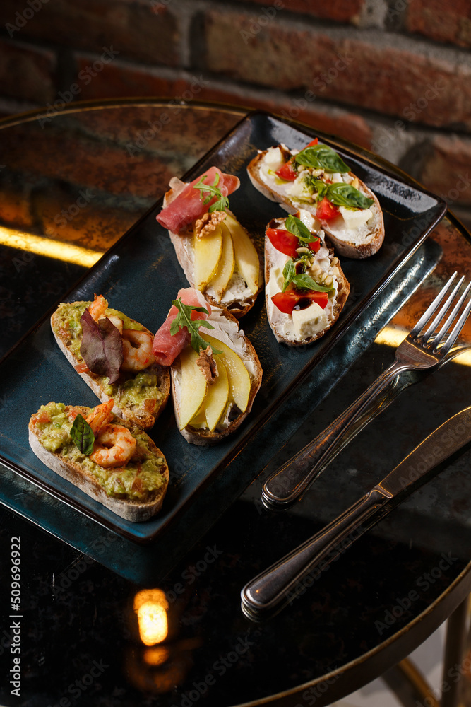 Bruschettas with vegetables. Start dishes with cherry tomatoes, avocado, cream cheese and shrimps. Food composition, tasty italian meal