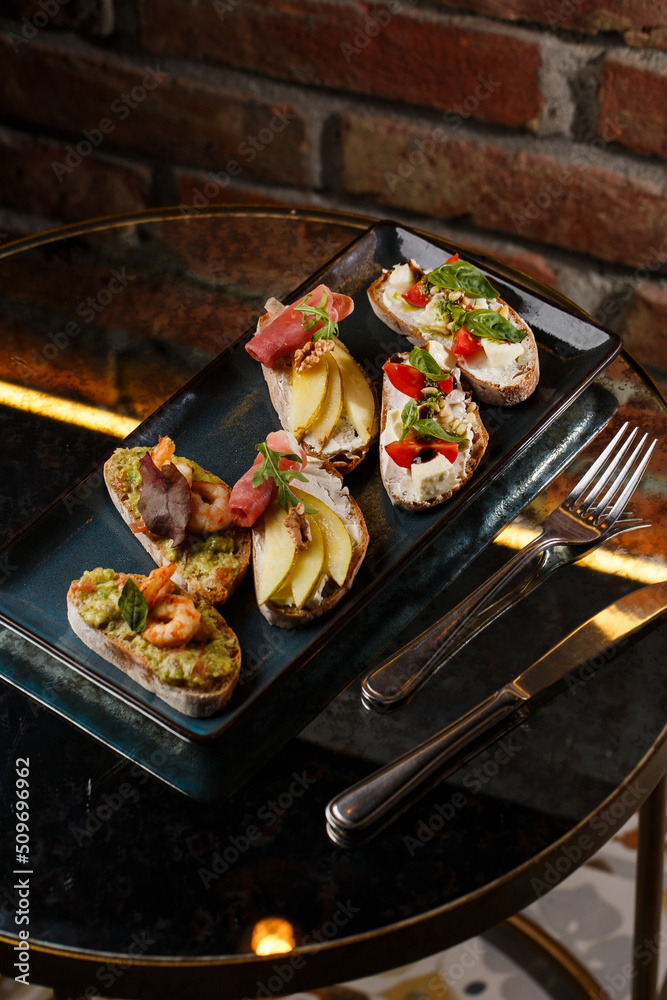 Bruschettas with vegetables. Start dishes with cherry tomatoes, avocado, cream cheese and shrimps. Food composition, tasty italian meal