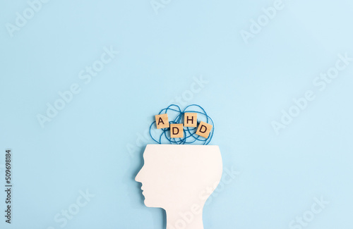 Silhouette of human head and wooden blocks with the letters ADHD on blue background. Minimal concept of attention deficit hyperactivity syndrome. Copy space photo