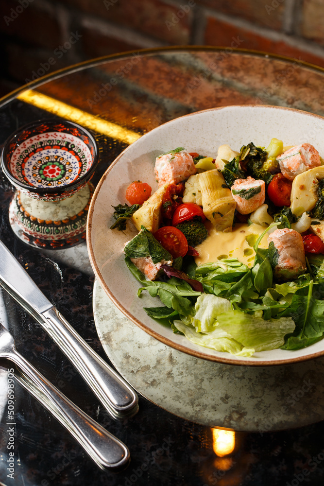A salad with grilled salmon, mashed avocado and lettuce dressed with cream cheese. Close-up of the dish in a brown bowl isolated on brown background.