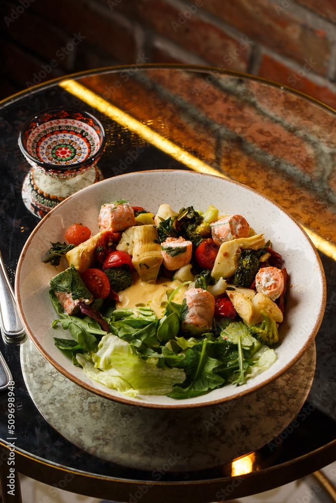 A salad with grilled salmon, mashed avocado and lettuce dressed with cream cheese. Close-up of the dish in a brown bowl isolated on brown background.