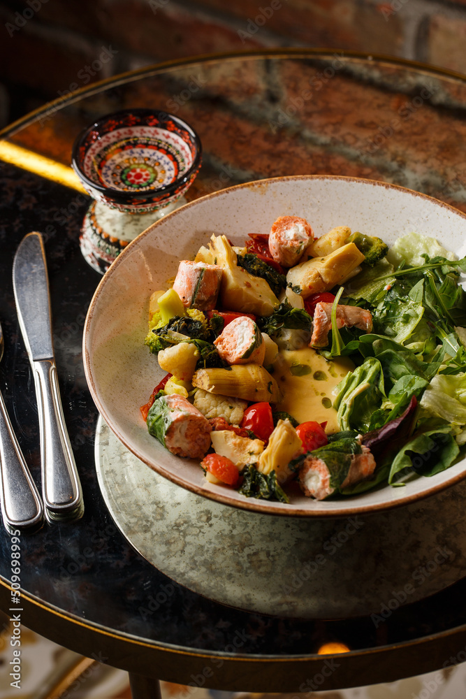 A salad with grilled salmon, mashed avocado and lettuce dressed with cream cheese. Close-up of the dish in a brown bowl isolated on brown background.