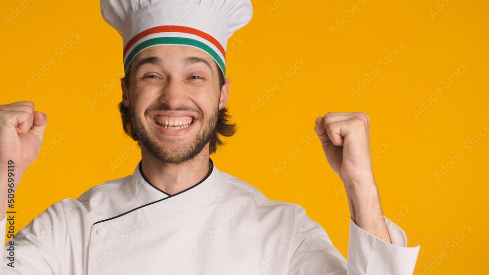 Close up successful chef wearing uniform rejoicing at camera over yellow background. Positive man in chef hat looking happy Close up successful chef wearing uniform rejoicing at camera over yellow background. Positive man in chef hat looking happy