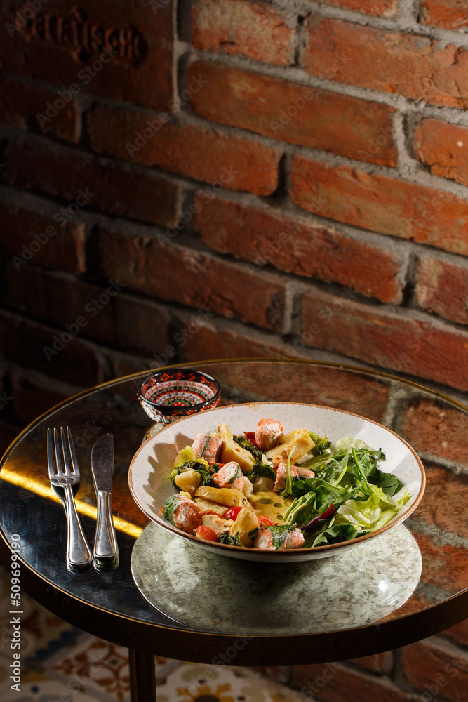 A salad with grilled salmon, mashed avocado and lettuce dressed with cream cheese. Close-up of the dish in a brown bowl isolated on brown background.