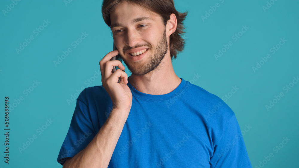 Close up attractive guy talking on smartphone with friend smiling at camera against a blue background. Communication concept Close up attractive guy talking on smartphone with friend smiling at camera against a blue background. Communication concept