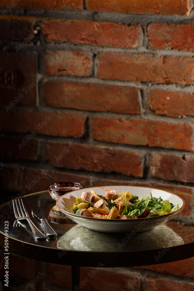 A salad with grilled salmon, mashed avocado and lettuce dressed with cream cheese. Close-up of the dish in a brown bowl isolated on brown background.