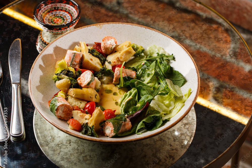 A salad with grilled salmon, mashed avocado and lettuce dressed with cream cheese. Close-up of the dish in a brown bowl isolated on brown background.