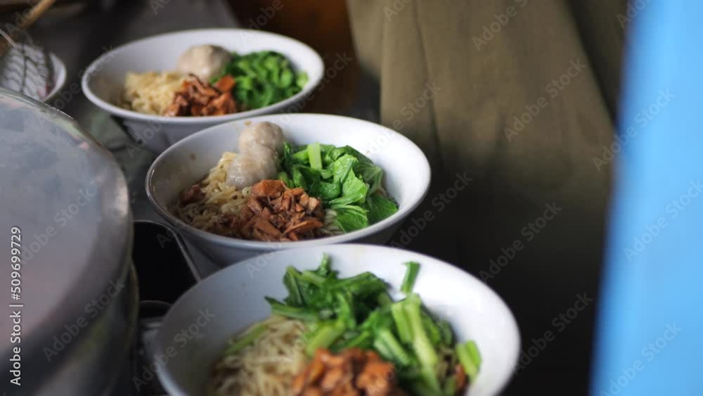 Making chicken noodles. View of a penjual mie ayam bakso or meatball chicken noodle seller who is making chicken noodles for the buyer. Selective focus. 